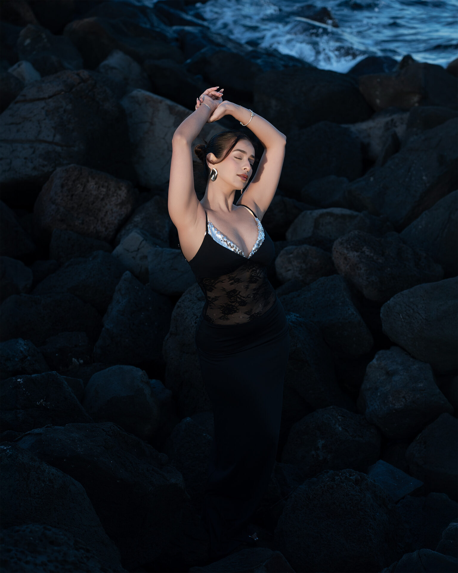 Outdoor editorial — arms raised on dark coastal rocks