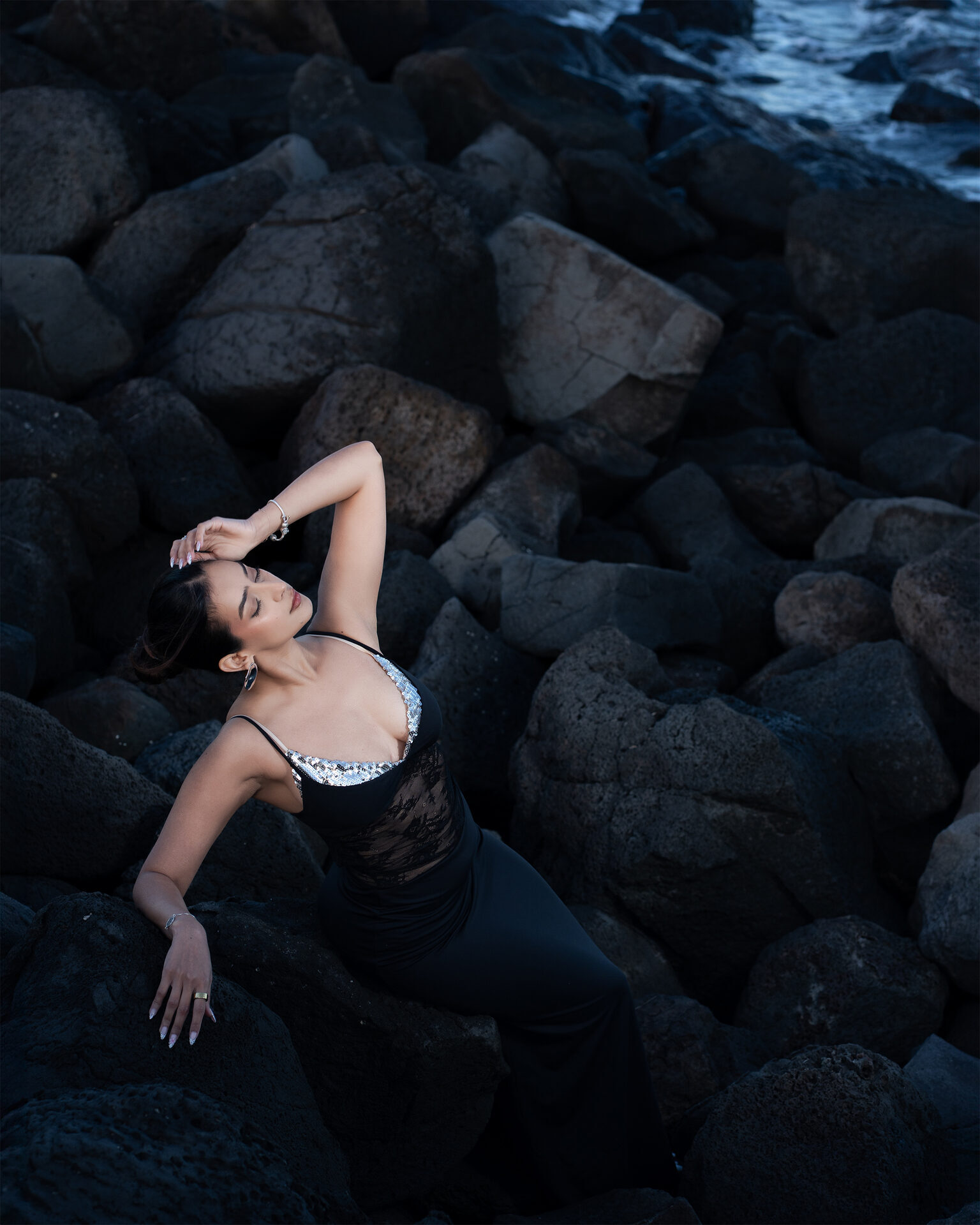 Outdoor editorial — wide reclining pose on coastal rocks with ocean
