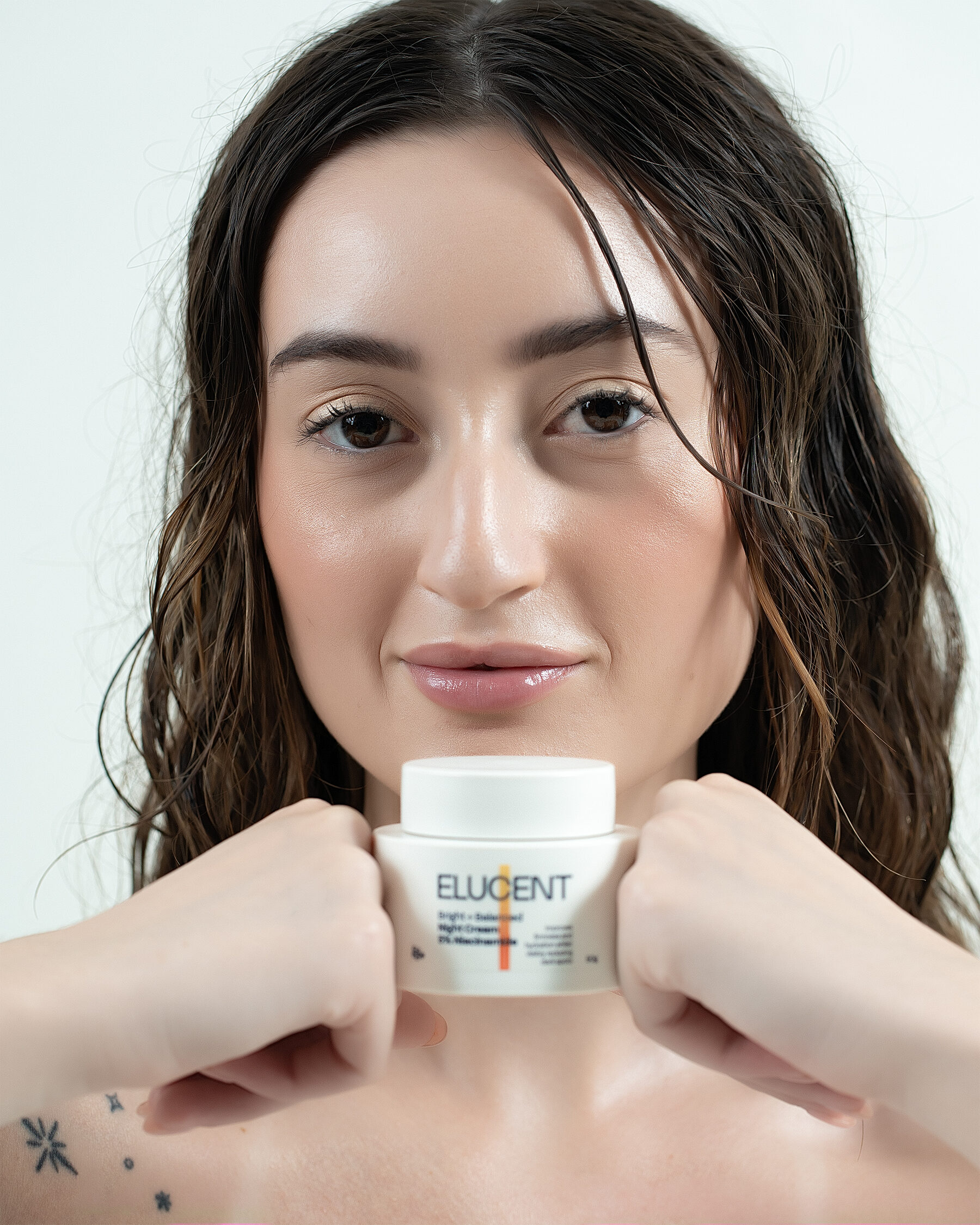 Elucent Night Cream — model holding jar, both hands, direct gaze