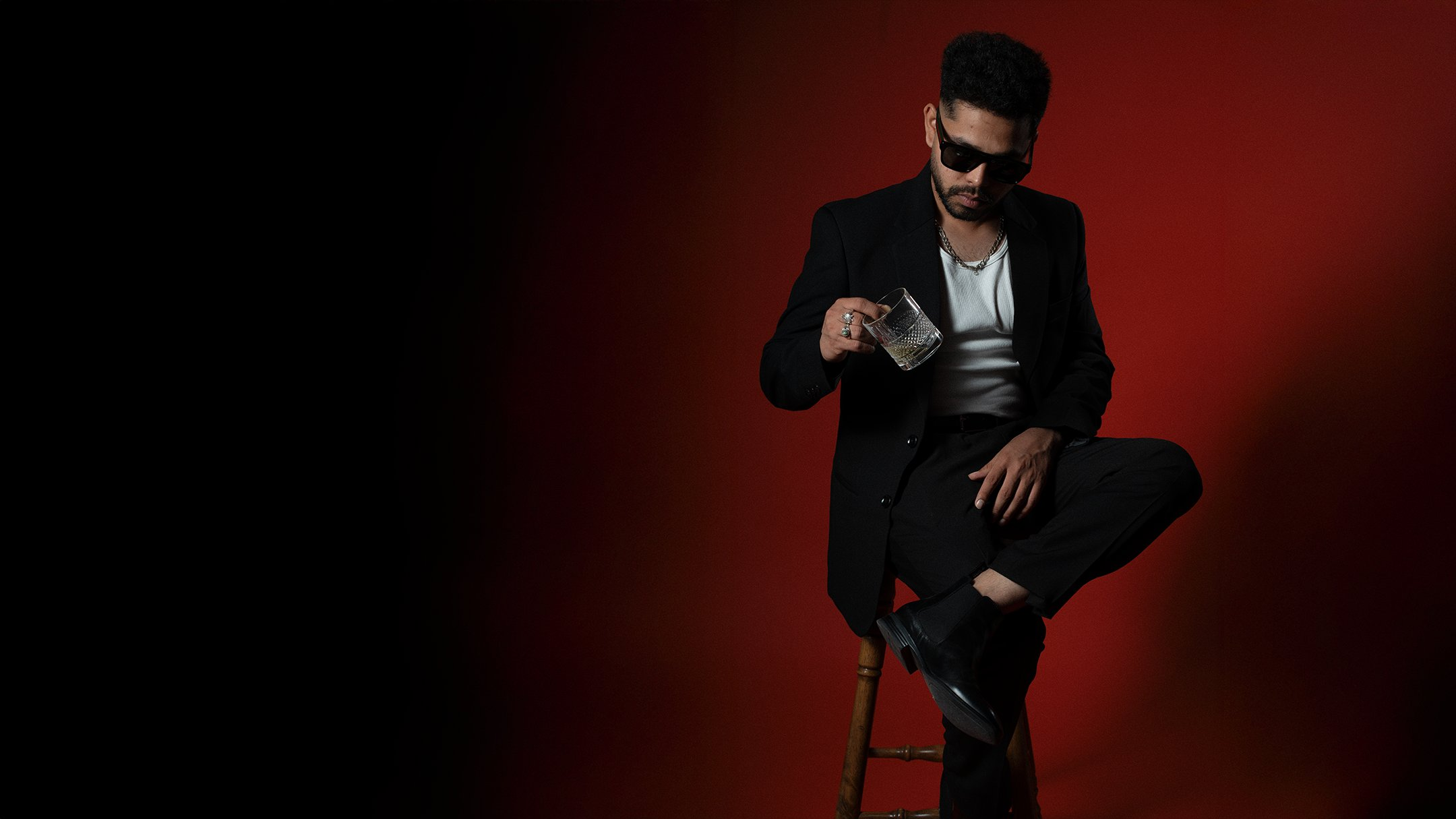 Male portrait — red backdrop seated with drink